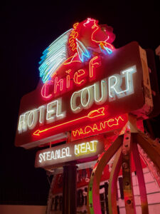 Photo of a vintage neon Chief Hotel Court sign, displaying vacancy and an amenity of steamed heat and depicting a Native American man with headdress