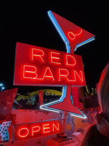 Photo of a vintage, lit-up neon sign for the Red Barn bar depicting a martini glass